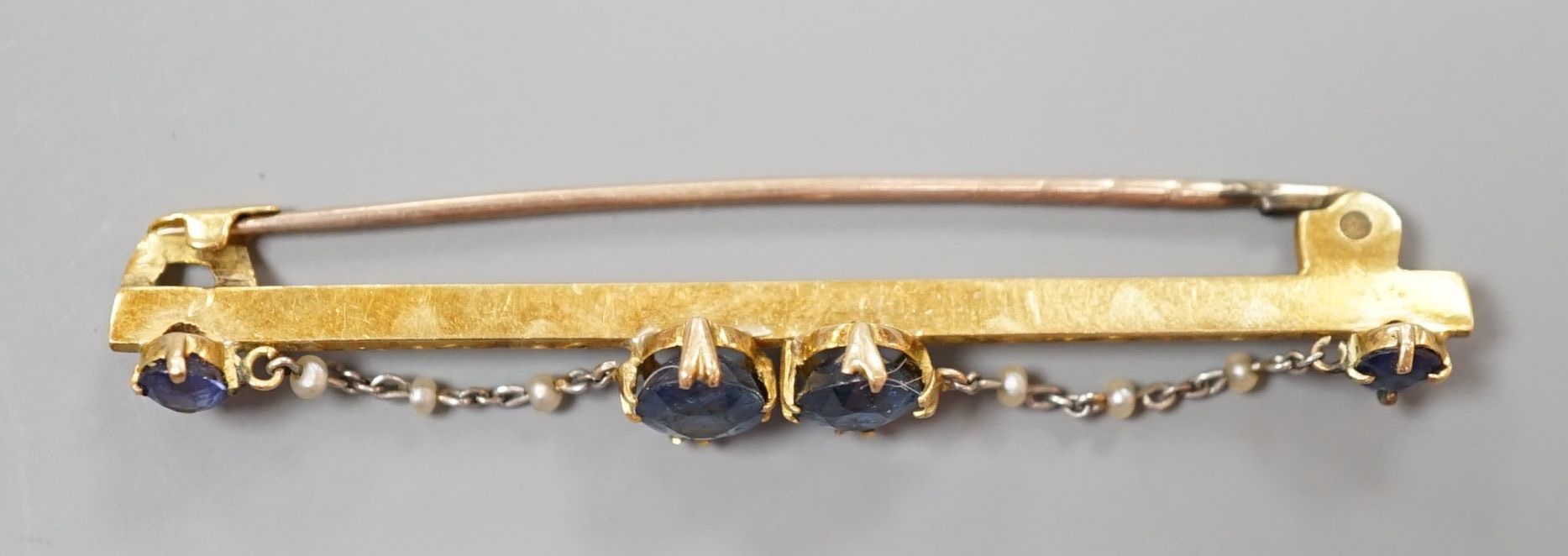 An early 20th century yellow metal sapphire and seed pearl set bar brooch, 61mm, gross weight 5.6 grams.